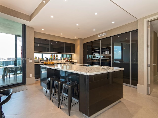 kitchen featuring a kitchen island, black electric cooktop, light stone countertops, a breakfast bar area, and oven