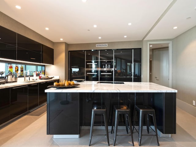 kitchen featuring sink, oven, light stone counters, a large island with sink, and a kitchen bar