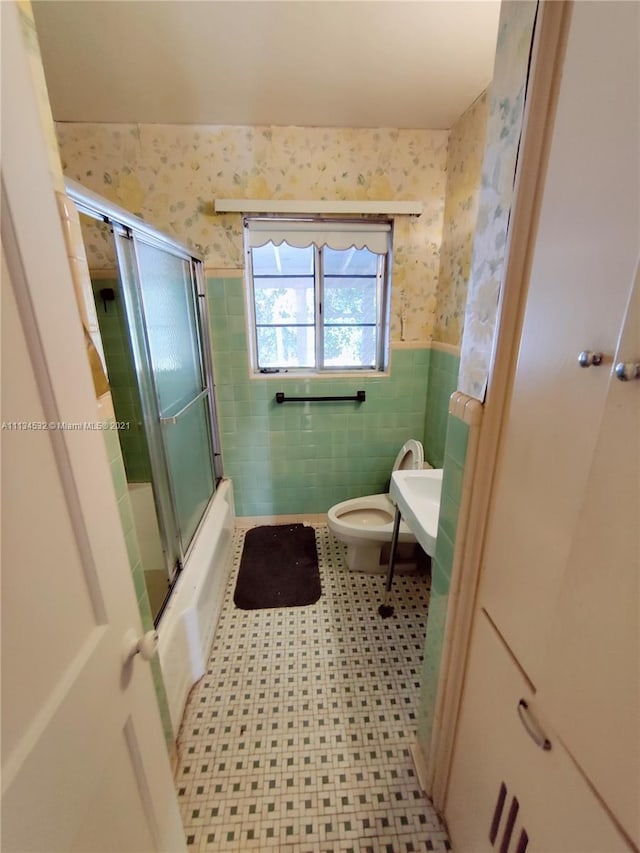 full bathroom with toilet, bath / shower combo with glass door, tile walls, tile floors, and sink