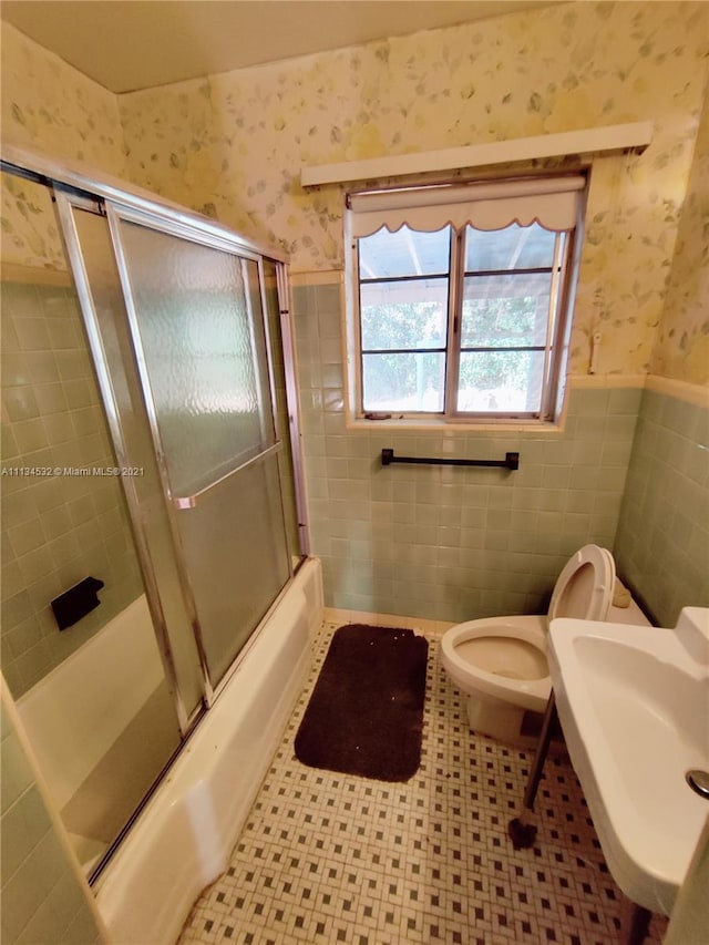 full bathroom featuring toilet, bath / shower combo with glass door, tile walls, tile flooring, and sink