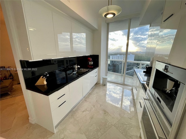 kitchen featuring light tile floors, white cabinets, decorative light fixtures, and a wall of windows