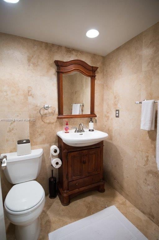 bathroom with toilet, tile flooring, vanity, and tile walls