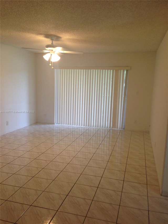 empty room featuring ceiling fan, light tile patterned floors, and a textured ceiling