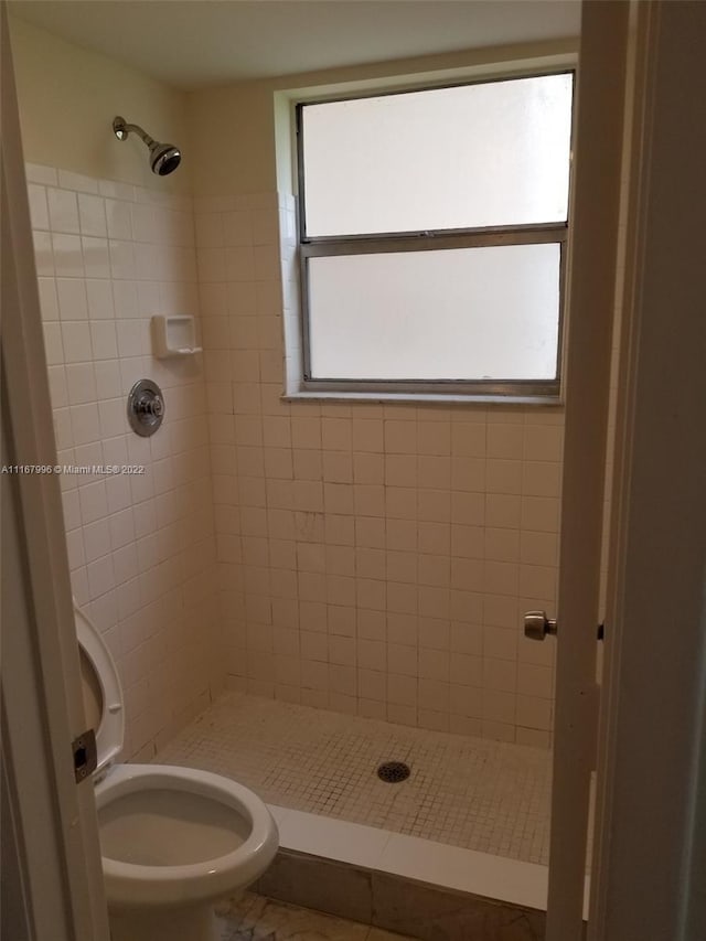 bathroom with tile patterned flooring, a tile shower, toilet, and a healthy amount of sunlight