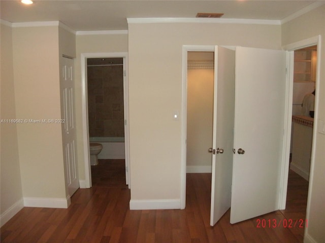 unfurnished bedroom featuring a walk in closet, ensuite bathroom, crown molding, and dark wood-type flooring