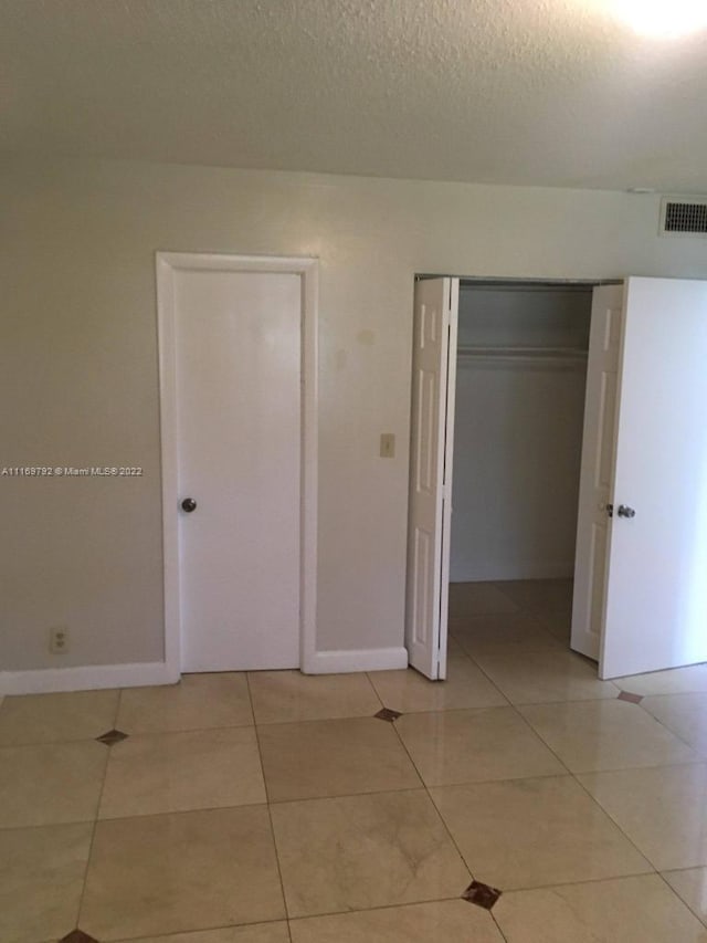 unfurnished bedroom featuring light tile patterned floors, a textured ceiling, and a closet