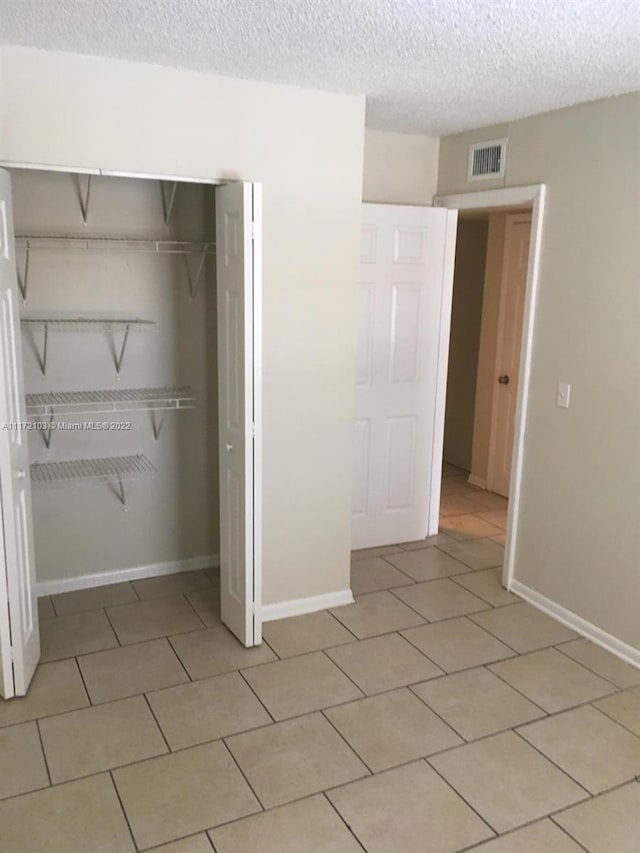 unfurnished bedroom featuring a closet, light tile patterned floors, and a textured ceiling