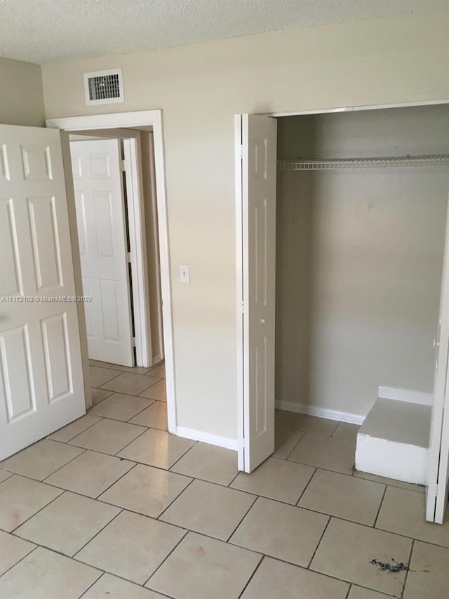 unfurnished bedroom with light tile patterned floors, a textured ceiling, and a closet