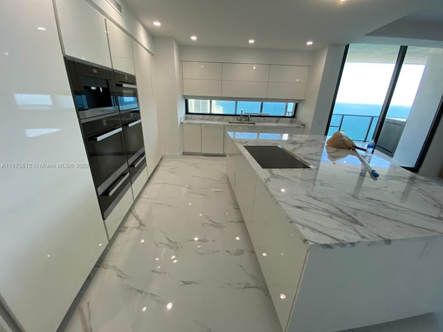 kitchen featuring light stone countertops, double oven, white cabinetry, and sink