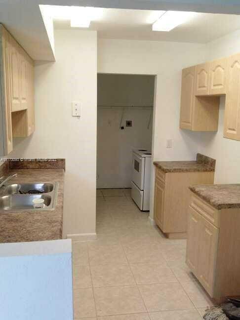 kitchen with white range with electric cooktop, light brown cabinets, light tile patterned flooring, and sink