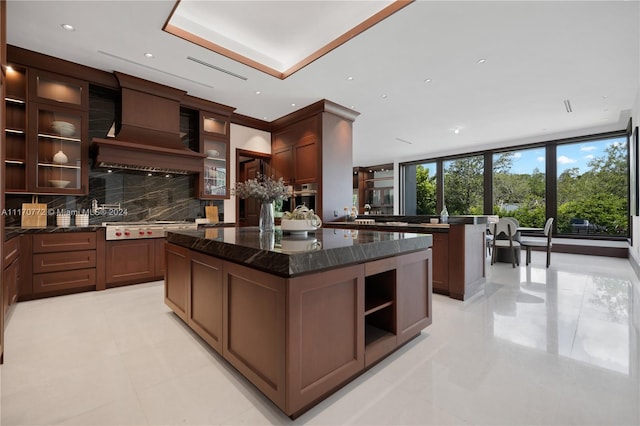 kitchen featuring a wall of windows, premium range hood, tasteful backsplash, a kitchen island, and dark stone counters