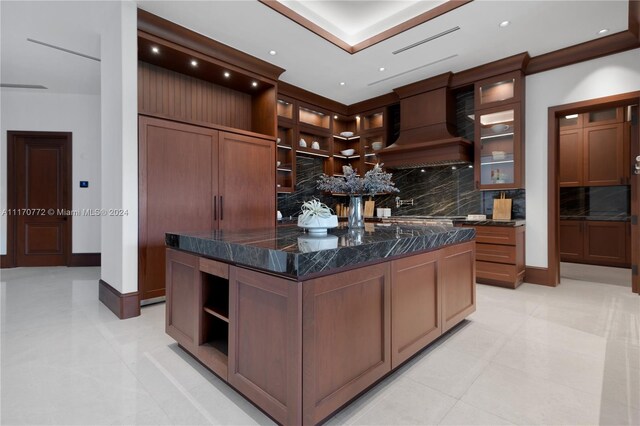 kitchen featuring custom exhaust hood, light tile patterned floors, a kitchen island, dark stone countertops, and decorative backsplash