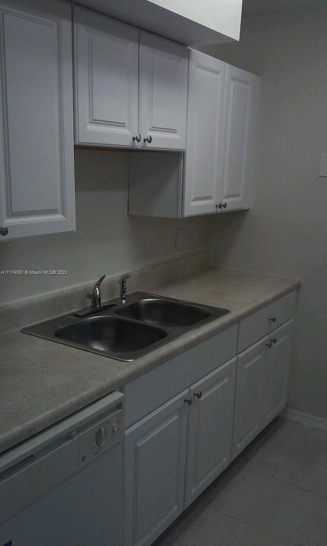 kitchen with white dishwasher, white cabinets, light tile patterned floors, and sink