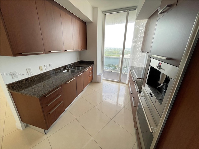 kitchen with stainless steel fridge, sink, floor to ceiling windows, dark stone countertops, and light tile flooring