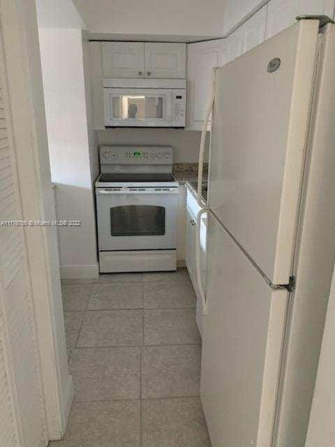 kitchen with white cabinets, light tile patterned floors, and white appliances