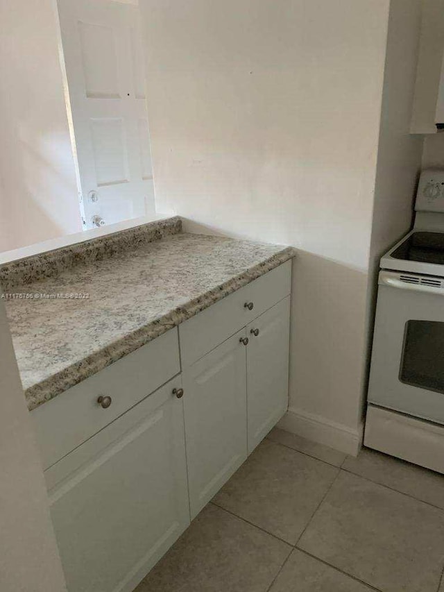 kitchen featuring electric range, light stone counters, white cabinetry, and light tile patterned floors