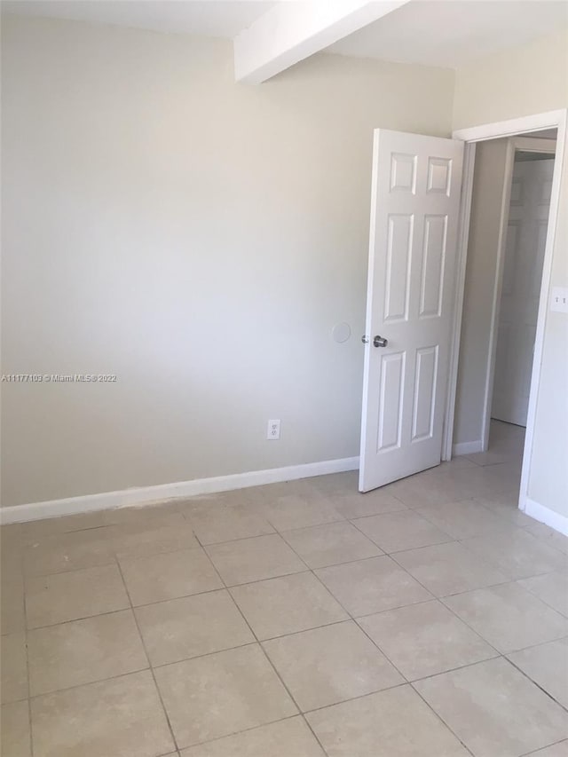 unfurnished room with beamed ceiling and light tile patterned floors