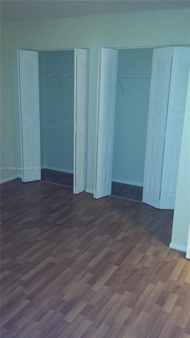 unfurnished bedroom with two closets and dark hardwood / wood-style floors