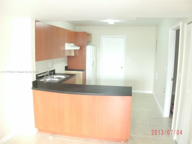 kitchen with kitchen peninsula, sink, light tile patterned floors, and white refrigerator with ice dispenser