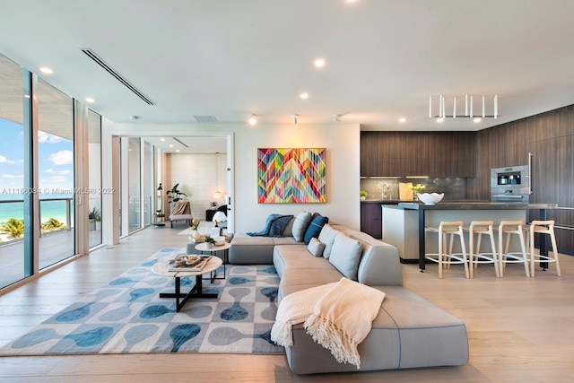 living room featuring floor to ceiling windows, light hardwood / wood-style floors, and a water view