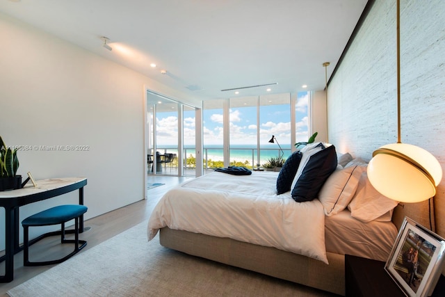 bedroom with access to exterior, light hardwood / wood-style flooring, a water view, and a wall of windows