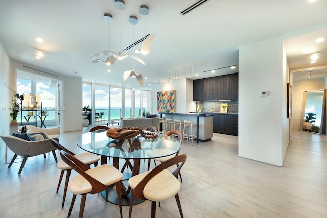 dining area with rail lighting, a water view, and light hardwood / wood-style flooring