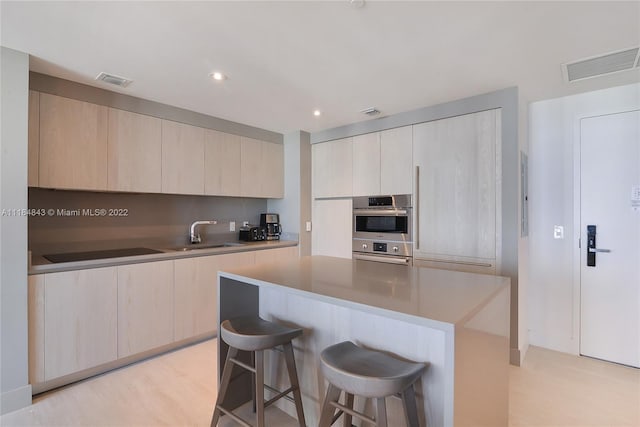 kitchen featuring stainless steel double oven, light hardwood / wood-style flooring, a kitchen island, and sink