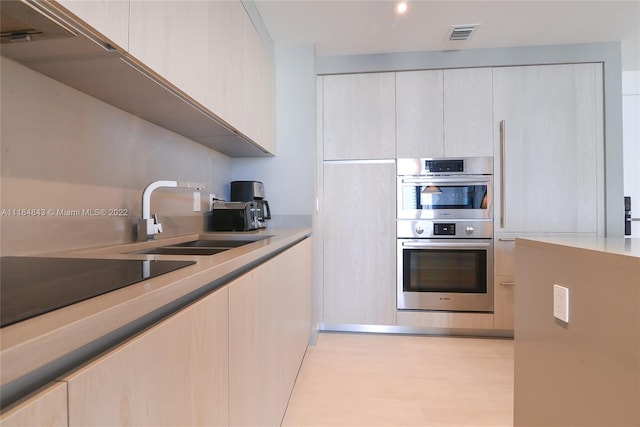 kitchen featuring stainless steel double oven, sink, and light hardwood / wood-style flooring