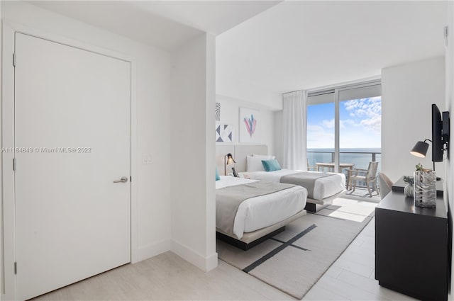 bedroom with access to outside, expansive windows, light hardwood / wood-style floors, and a water view