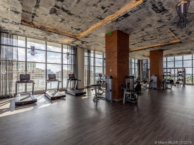 gym with floor to ceiling windows, brick wall, and dark wood-type flooring