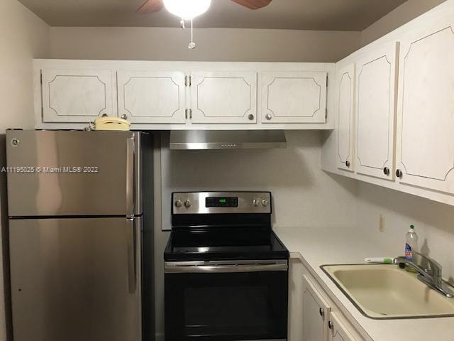 kitchen featuring wall chimney range hood, white cabinetry, ceiling fan, and appliances with stainless steel finishes