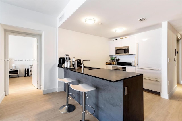 kitchen featuring a kitchen bar, light hardwood / wood-style flooring, white cabinetry, oven, and sink