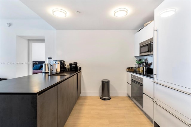 kitchen with kitchen peninsula, sink, white cabinets, stainless steel appliances, and light wood-type flooring