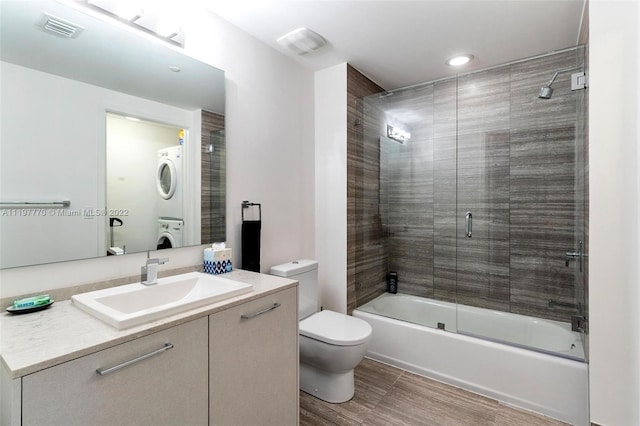 full bathroom featuring toilet, tile floors, stacked washer and clothes dryer, oversized vanity, and bath / shower combo with glass door