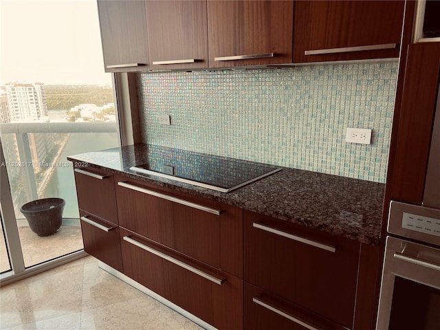 kitchen featuring light tile flooring, stainless steel oven, dark stone countertops, and black electric stovetop