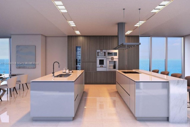 kitchen featuring a water view, a center island with sink, sink, and wall chimney range hood