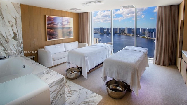 carpeted bedroom with wooden walls, access to outside, a wall of windows, and a water view