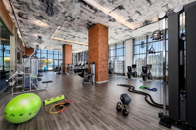 workout area featuring brick wall, expansive windows, and dark hardwood / wood-style flooring