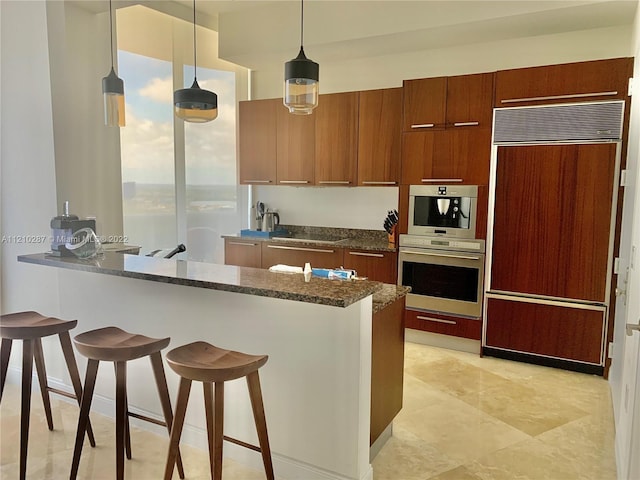 kitchen featuring hanging light fixtures, dark stone countertops, light tile floors, paneled fridge, and a breakfast bar area