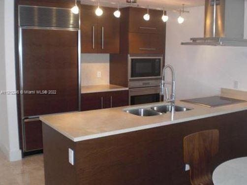 kitchen with exhaust hood, pendant lighting, stainless steel appliances, and sink