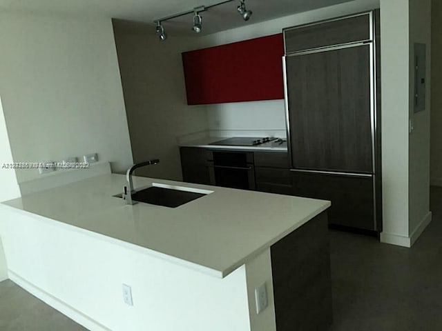 kitchen featuring paneled refrigerator, kitchen peninsula, sink, rail lighting, and black electric stovetop