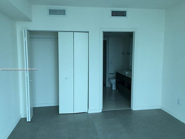 unfurnished bedroom with connected bathroom, a closet, and dark tile floors