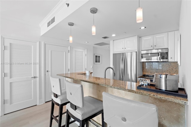 kitchen featuring backsplash, white cabinets, hanging light fixtures, light stone countertops, and appliances with stainless steel finishes