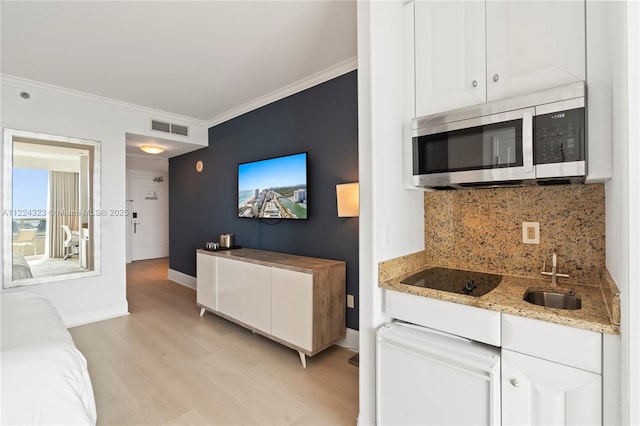 kitchen with white cabinets, black electric stovetop, sink, ornamental molding, and light stone counters