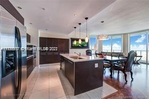 kitchen with stainless steel fridge, pendant lighting, light tile floors, a center island with sink, and dark brown cabinetry