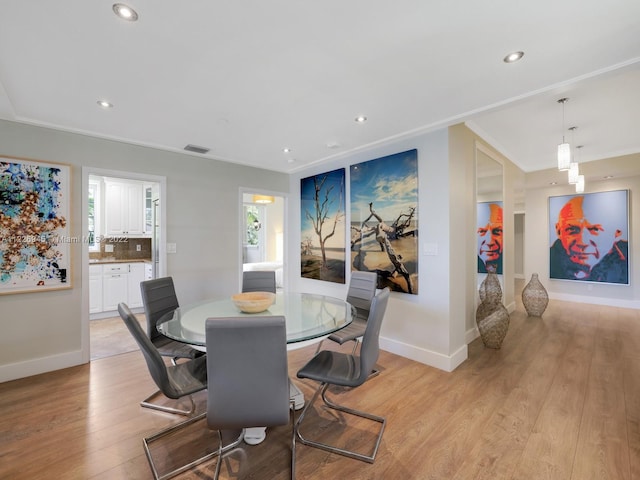 dining space with ornamental molding and light hardwood / wood-style flooring