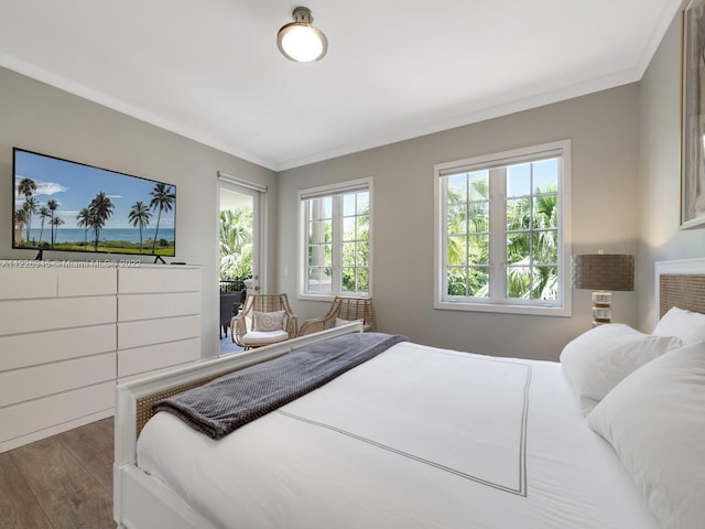 bedroom featuring multiple windows, wood-type flooring, a water view, and ornamental molding