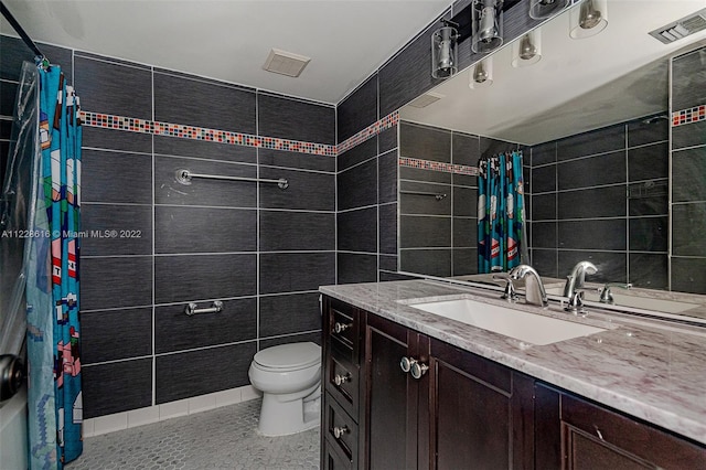 bathroom featuring vanity with extensive cabinet space, toilet, and tile walls