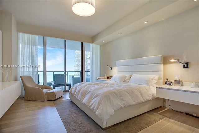 bedroom with hardwood / wood-style floors, expansive windows, access to exterior, and a water view