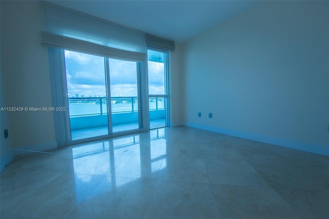 spare room featuring a water view, a wall of windows, and light tile floors